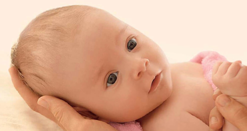 A close-up of a baby's face, with a hand gently cradling the baby's head.