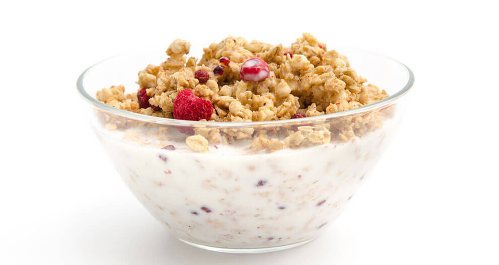 A transparent bowl filled with granola and dotted with red berries, set against a white background.