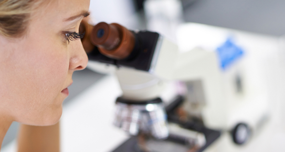 A woman is looking through a microscope.